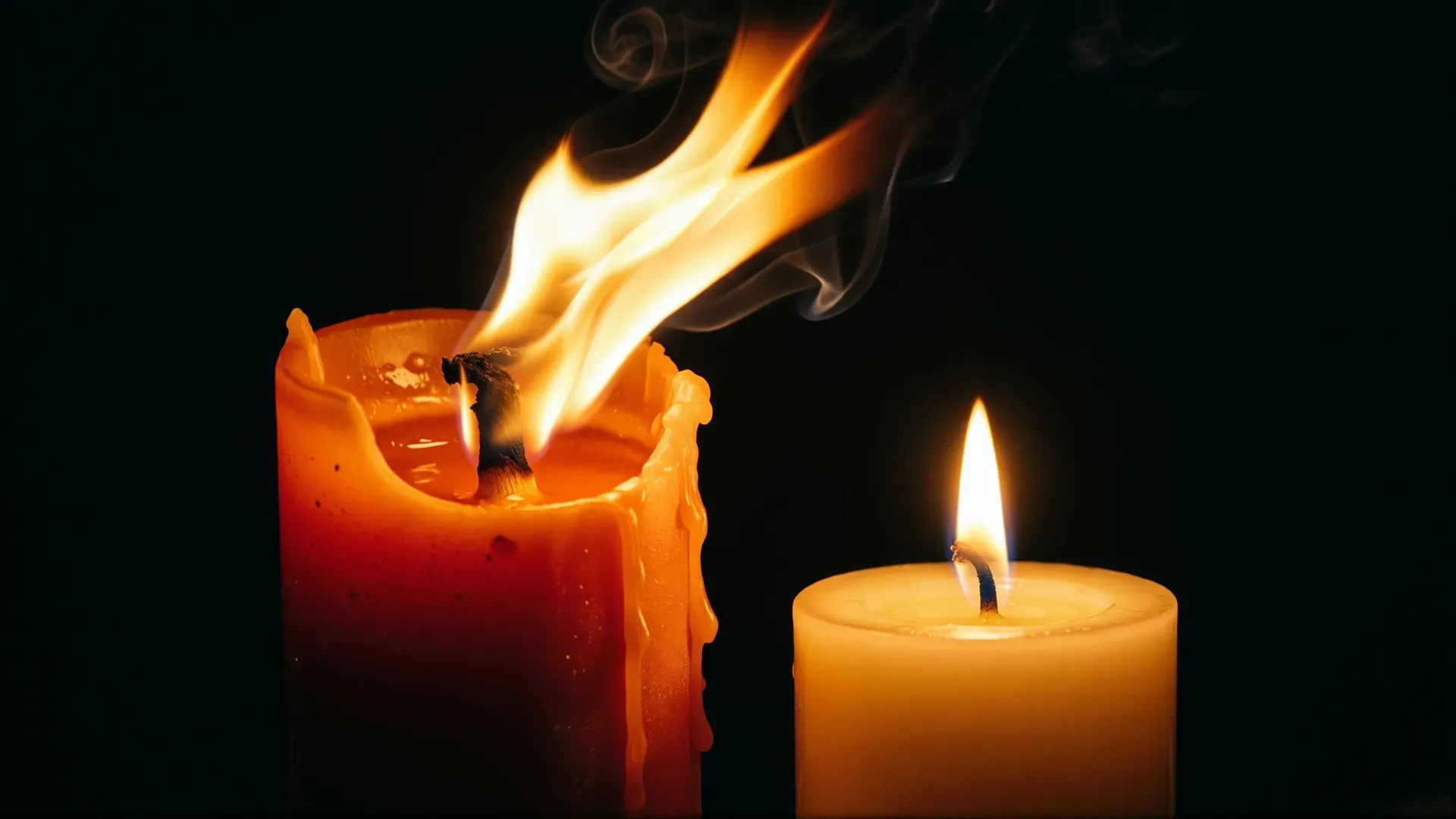 Two lit candles against black — one larger flame flickering wildly and dripping wax, the other a small steady flame, contrasting passionate and constant love
